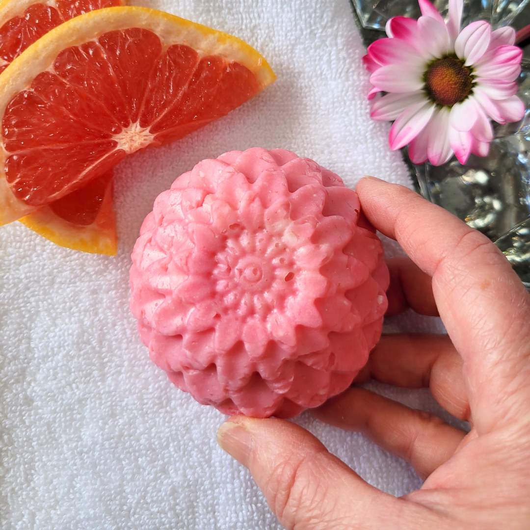 Hand reaching for Caley-Beth Pink Grapefruit and Palmarosa Body Wash Bar — a natural, soap-free, pH-balanced cleanser for sensitive skin, shown on a white towel in a bathroom setting.