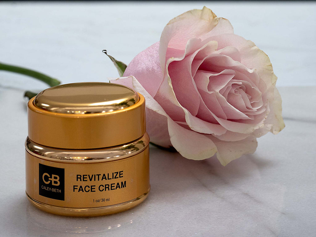 Caley-Beth Revitalizing Face Cream in gold jar next to a rose.