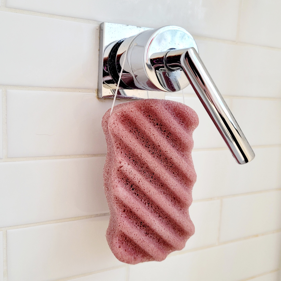Caley-Beth eco-friendly all-natural Konjac Body & Face sponge in French red clay hanging from a bathroom faucet.