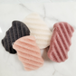 A flat lay of four natural Konjac Sponges in four colours; Black bamboo charcoal, White natural, Light pink cherry blossom, and Pink/Red French Red clay., made in Canada, perfect for gentle exfoliation and deep cleansing.

